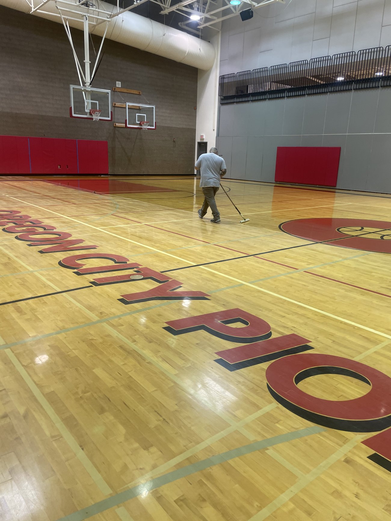 Worker applying gym floor finish with a T-bar applicator on the Oregon City Pioneers court