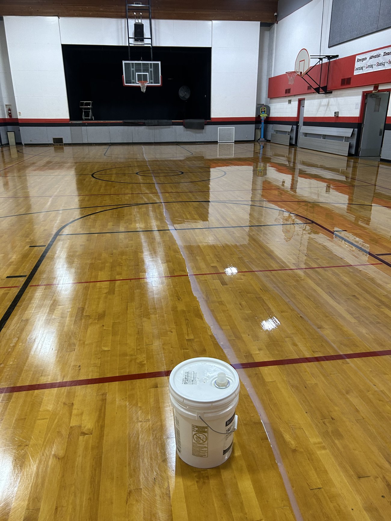 Fresh finish coat being applied to a wood gymnasium floor at Rivergate Adventist Elementary